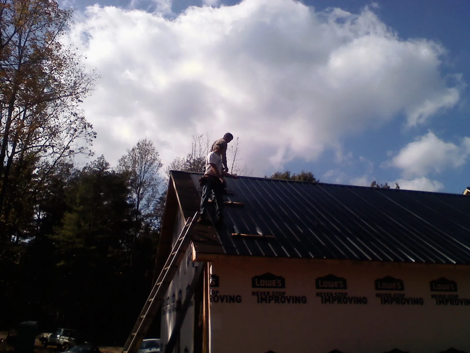 Roofer fastening dark metal panels high against a cloudy sky, from a Roof Inspection job in Pacifica